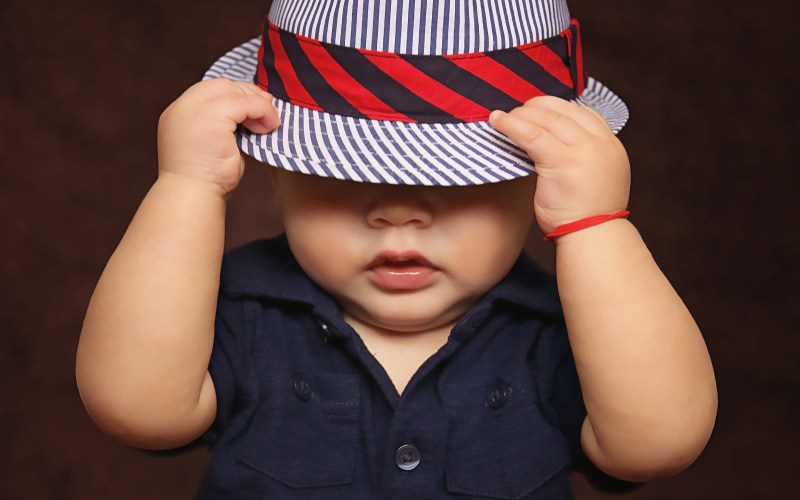 Baby wearing striped hat with hands holding it over eyes